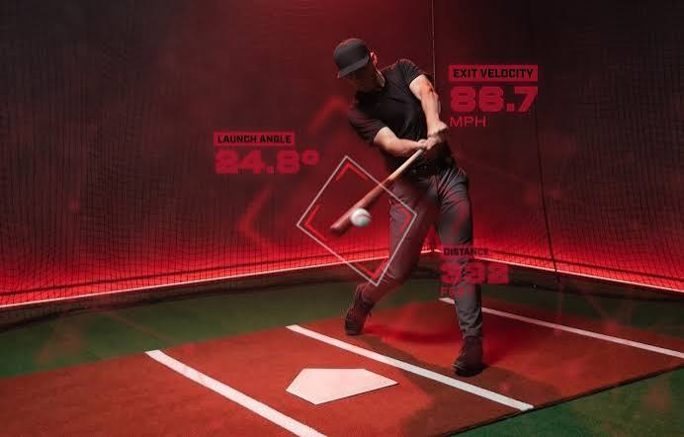 Hitter mid-swing in the cage with a HitTrax readout showing launch angle, exit velocity and distance